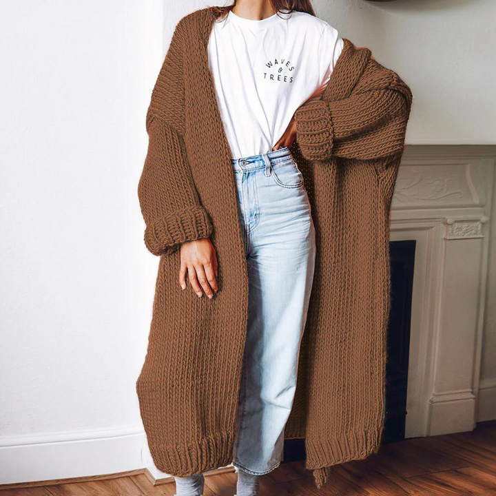 Vrouw draagt lange, bruine gebreide cardigan over witte T-shirt en blauwe jeans. Stijlvolle herfstmode, comfortabele dameskleding, casual outfit.