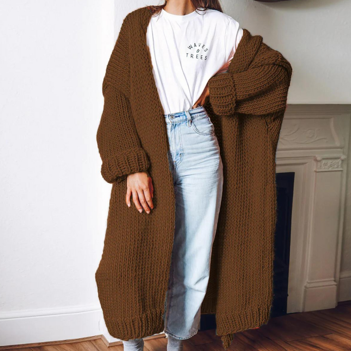 Vrouw in bruine gebreide lange cardigan, witte T-shirt en blauwe jeans, casual herfstmode, comfortabele dameskleding, trendy outfit.