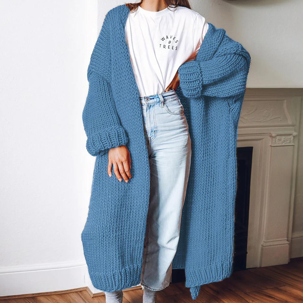 Vrouw draagt een lange, gebreide blauwe cardigan over een wit T-shirt en lichte spijkerbroek. Stijlvolle herfstmode, comfortabele dameskleding.