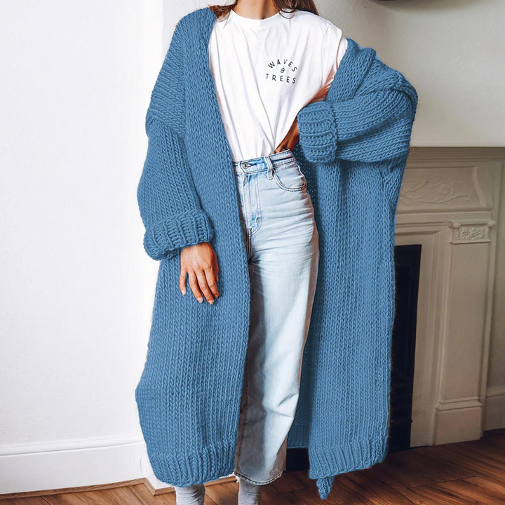 Vrouw draagt een lange, gebreide blauwe cardigan over een wit T-shirt en lichte spijkerbroek. Stijlvolle herfstmode, comfortabele dameskleding.
