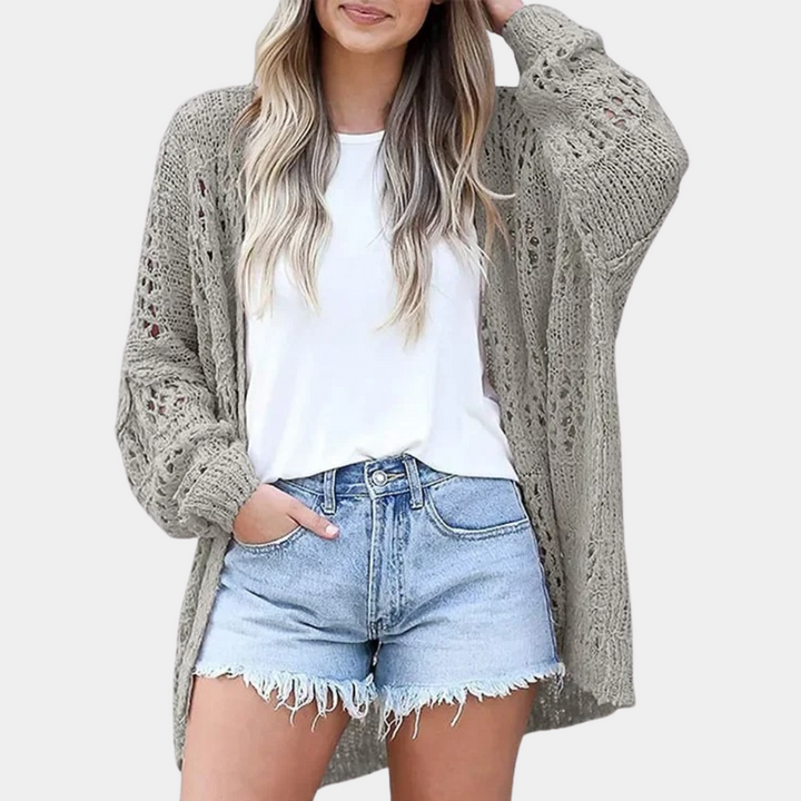 Grijze gebreide damesvest, opengewerkt patroon, casual stijl, gedragen met witte top en denim shorts. Perfect voor lente- en zomermode.