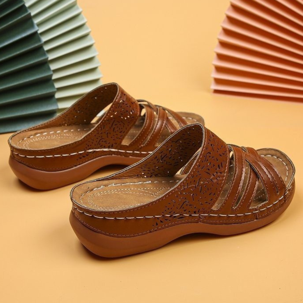 Lichtbruine leren sandalen met open teen en geperforeerd bloemmotief, comfortabele zool, op een beige achtergrond met decoratieve waaiers.