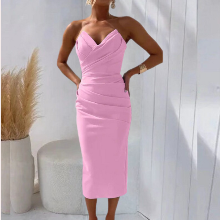 Vrouw in roze bodycon jurk met spaghetti bandjes, staand voor witte achtergrond. Trendy damesmode, elegante avondjurk, zomeroutfit.