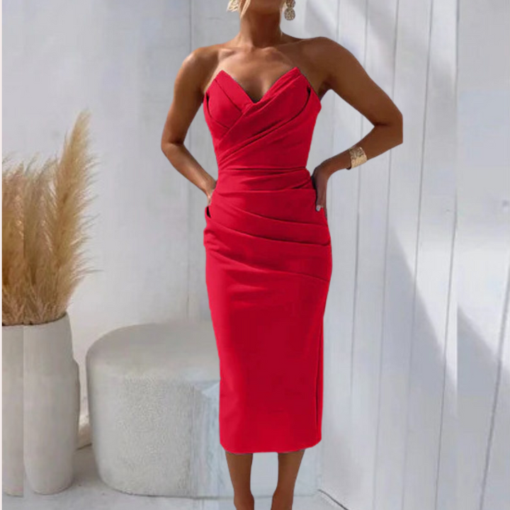 Vrouw in elegante rode cocktailjurk met hartvormige halslijn, staand in moderne witte ruimte met decoratieve pampasgras. Perfect voor avondkleding.