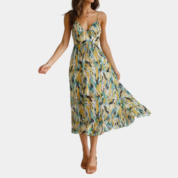 Vrouw in zomerse maxi-jurk met groene, gele en blauwe bladerenprint, spaghetti bandjes en vloeiende rok. Perfect voor casual en strandoutfits.