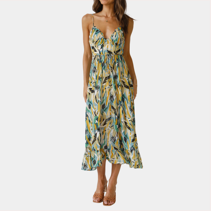 Vrouw in zomerse maxi-jurk met groene en gele bladprint, spaghetti bandjes en V-hals. Perfect voor casual en strandoutfits.
