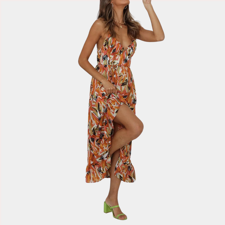 Oranje zomerjurk met kleurrijke bloemenprint, diepe V-hals en hoge split. Perfect voor strandmode en zomerse evenementen. Vrouw draagt groene sandalen.
