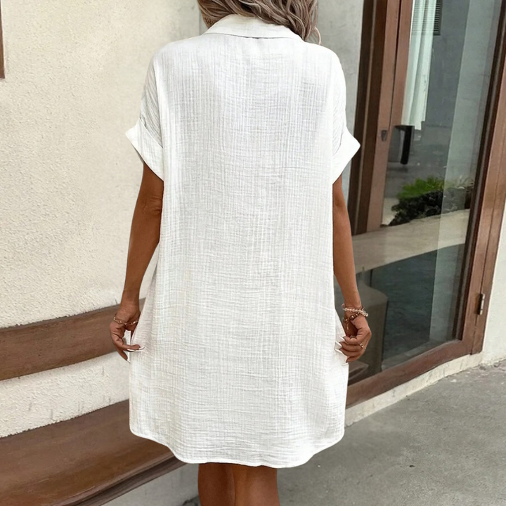 Vrouw in witte katoenen zomerjurk met korte mouwen, staand voor een houten bank. Perfect voor casual en zomerse mode.