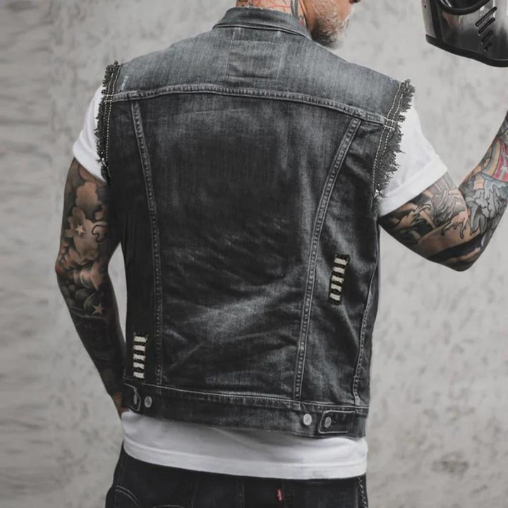 Man in versleten denim spijkerjack met tatoeages, rugaanzicht. Modieuze streetwear, casual stijl. Grijze achtergrond.