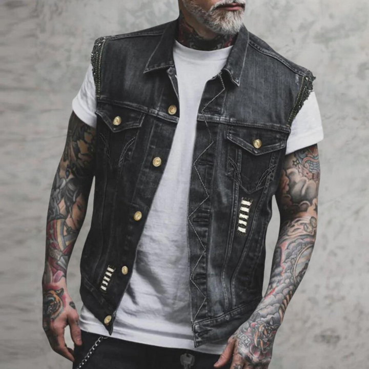 Man met getatoeëerde armen draagt een zwarte spijkerhes met gouden knopen en witte T-shirt. Modieuze herenkleding, streetwear stijl.
