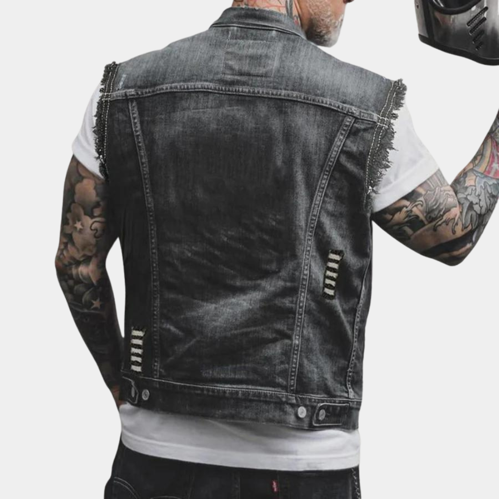 Man in zwart denim spijkerjack zonder mouwen, met tatoeages op armen, houdt motorhelm vast. Modieuze herenkleding, casual streetwear.