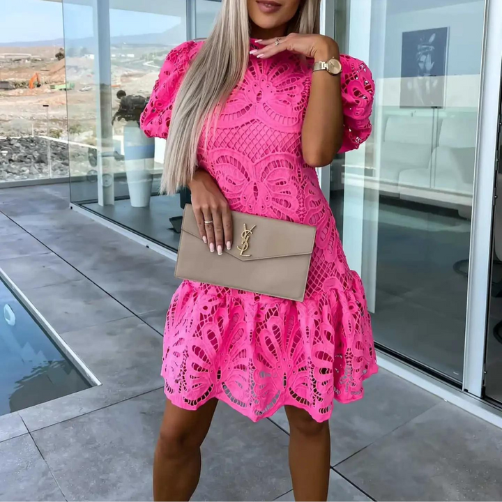 Vrouw in roze kanten jurk met beige designer clutch, staand op moderne patio. Zomermode, elegante stijl, trendy kleding.