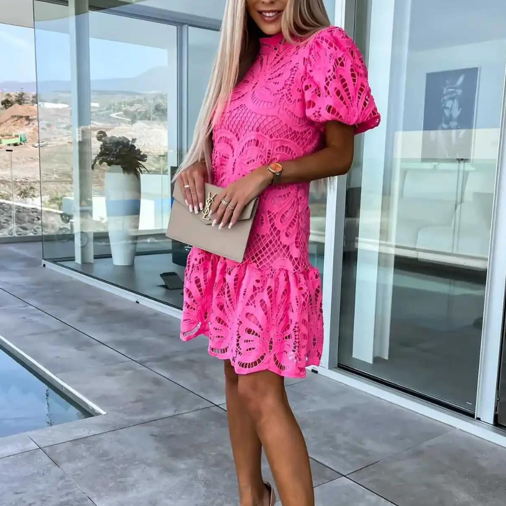 Vrouw in roze kanten jurk met clutch, staand op moderne patio. Zomermode, elegante kleding, trendy outfit, buitenomgeving.
