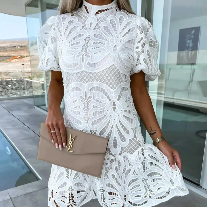 Vrouw in witte kanten jurk met korte mouwen, houdt een beige designer clutch vast. Moderne achtergrond, zomerse mode, elegante stijl.
