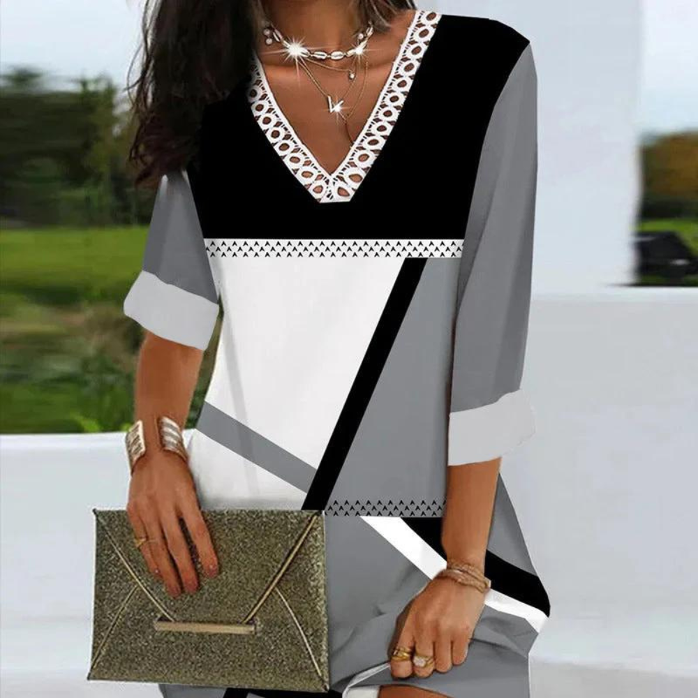 Vrouw in stijlvolle zwart-wit-grijze jurk met geometrisch patroon, draagt gouden clutch en sieraden. Perfect voor mode en accessoires SEO.