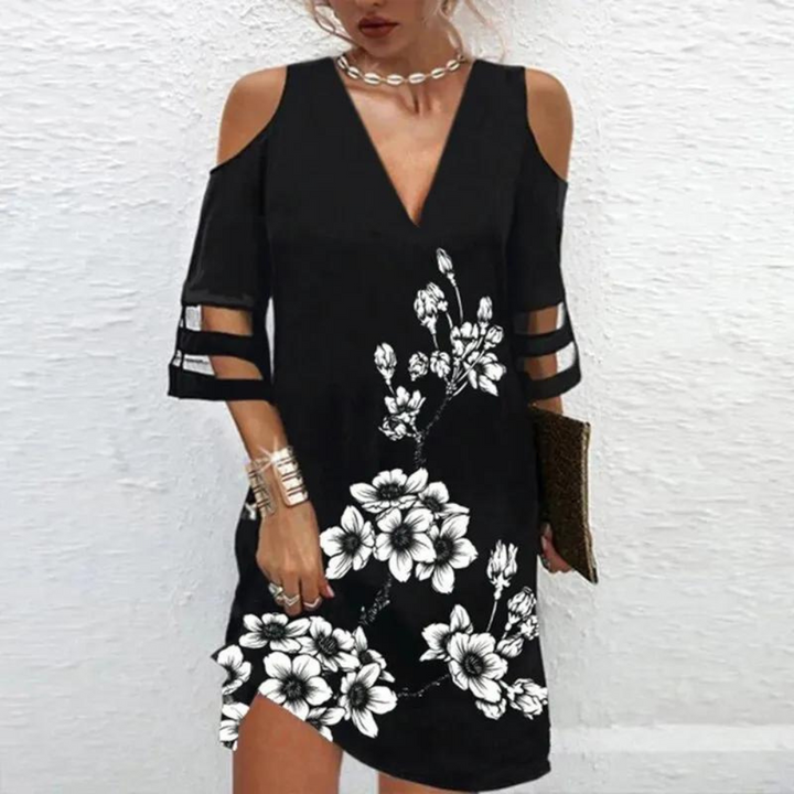 Zwarte jurk met bloemenprint, open schouders en driekwart mouwen. Perfect voor zomeravonden. Trendy damesmode, elegante casual stijl.