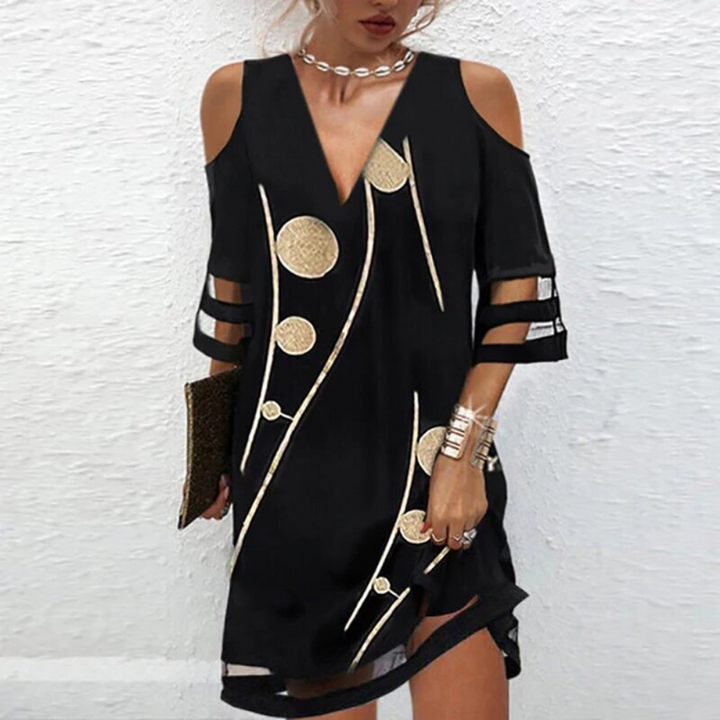 Zwarte jurk met gouden cirkelpatronen, open schouders en transparante mouwen. Elegante damesmode, perfect voor avondkleding en feestelijke gelegenheden.