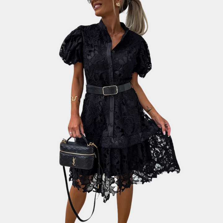 Vrouw in zwarte kanten jurk met pofmouwen en riem, houdt een stijlvolle zwarte handtas vast. Elegante mode, trendy dameskleding.