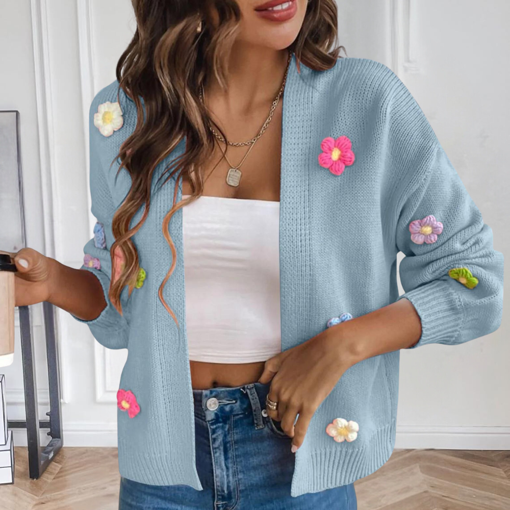Vrouw in blauwe gebreide cardigan met kleurrijke bloemen, witte top en spijkerbroek, houdt een koffiebeker vast. Trendy damesmode, casual outfit.