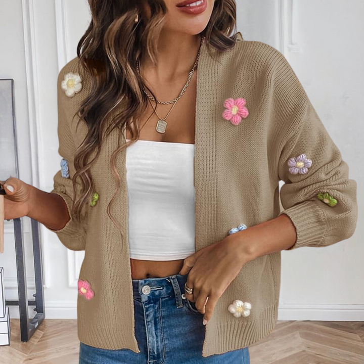 Vrouw draagt beige gebreid vest met kleurrijke bloemen, witte top en blauwe jeans. Trendy damesmode, casual outfit, herfstkleding.