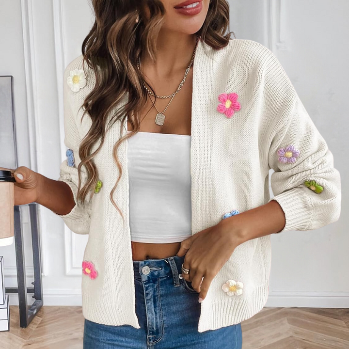 Vrouw draagt witte gebreide cardigan met kleurrijke bloemen, witte crop top en blauwe jeans. Trendy damesmode, casual outfit, herfststijl.