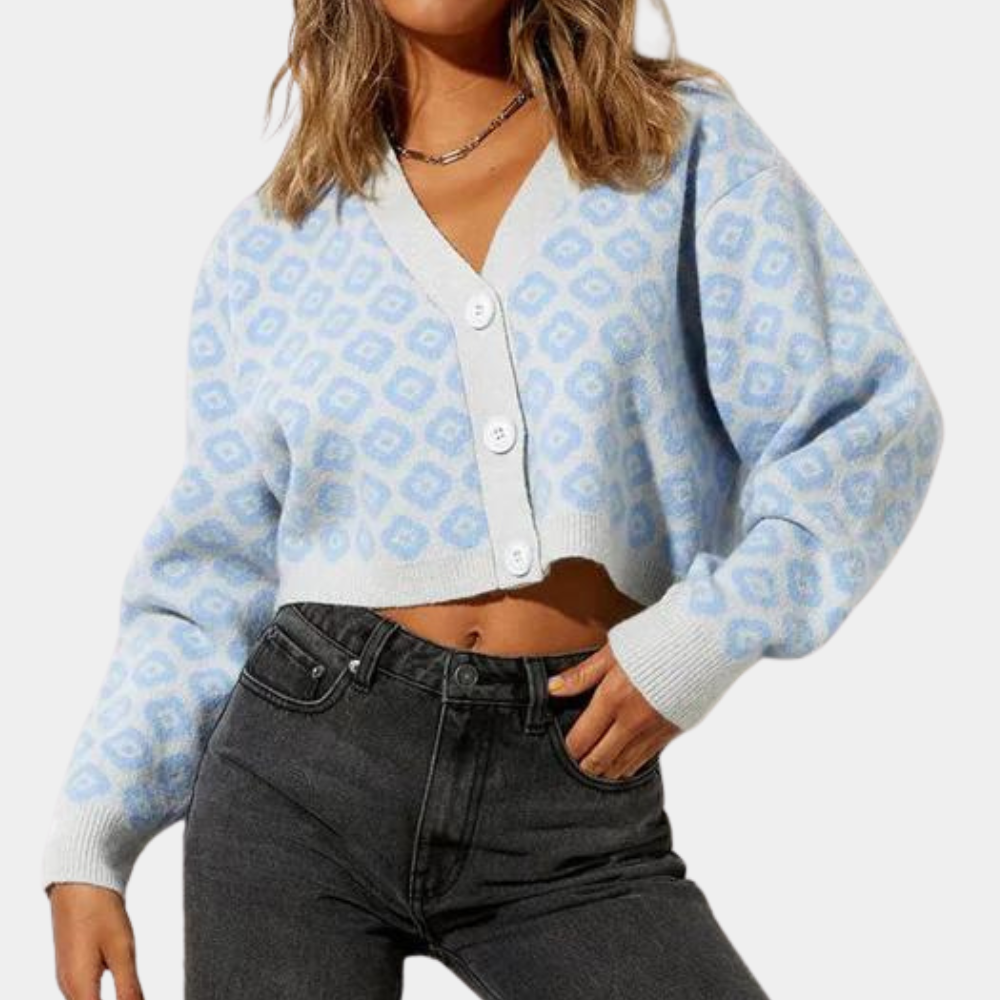 Vrouw draagt lichtblauw gebreid vest met witte knopen en geometrisch patroon, gecombineerd met zwarte jeans. Modieuze dameskleding, casual stijl.