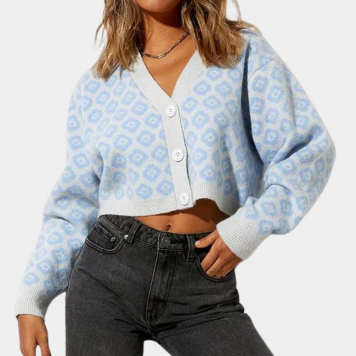 Vrouw draagt lichtblauw gebreid vest met witte knopen en geometrisch patroon, gecombineerd met zwarte jeans. Modieuze dameskleding, casual stijl.