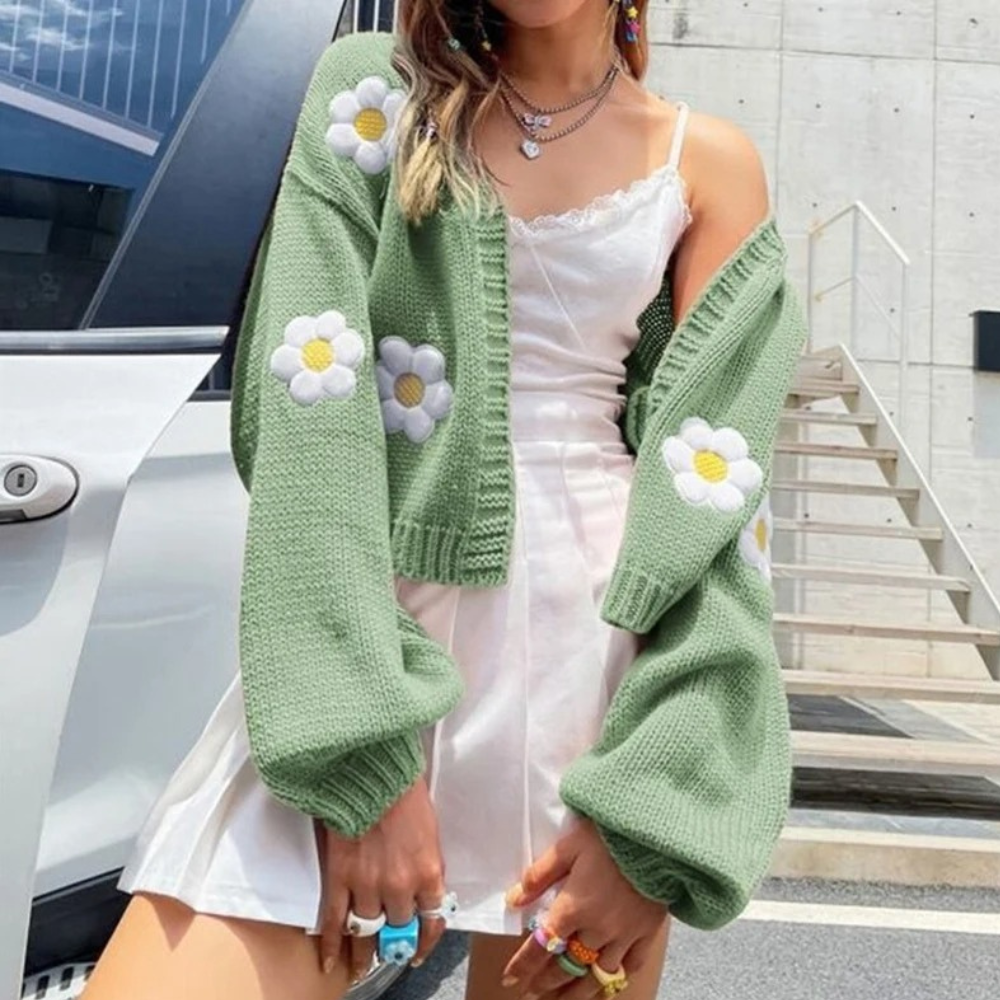 Groene gebreide cardigan met madeliefjes, gedragen over een witte jurk. Trendy damesmode, lente/zomer outfit, casual en stijlvol.