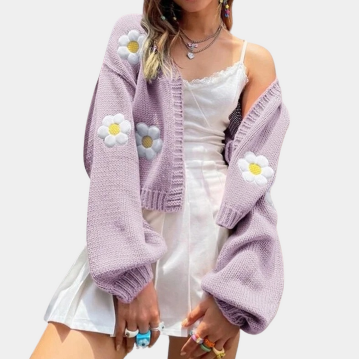 Vrouw in witte jurk met lila gebreid vest met madeliefjes, trendy mode, kleurrijke ringen, casual lente-zomer outfit.