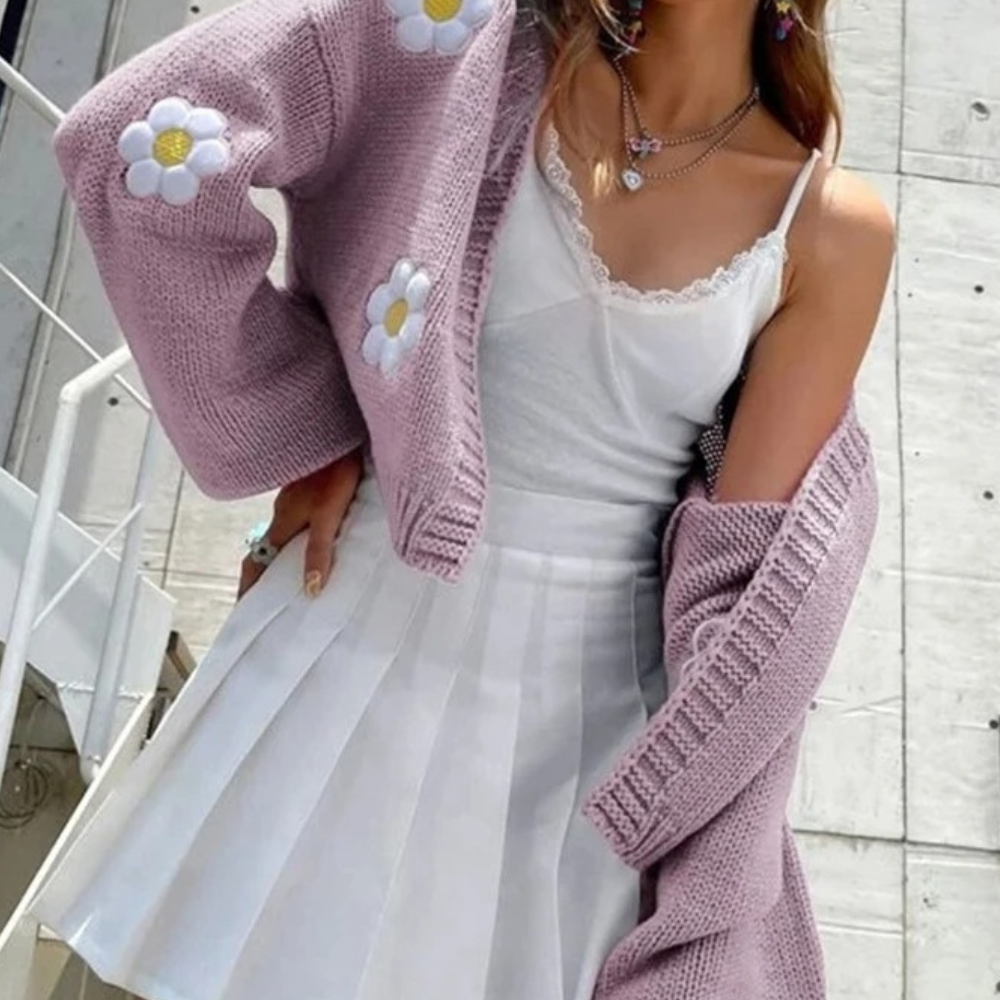 Vrouw in lila gebreid vest met madeliefjes, witte kanten top en geplooide rok. Trendy damesmode, lente outfit, casual chique stijl.