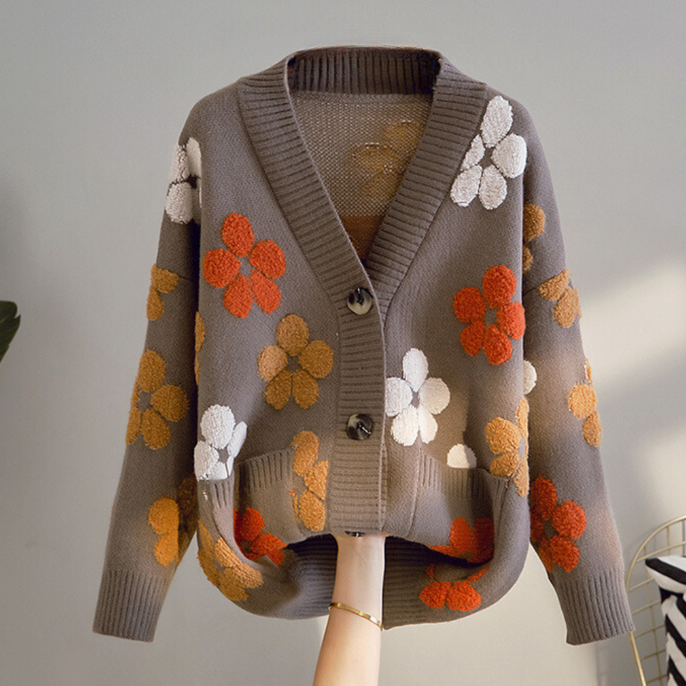 Grijze damestrui met bloemenpatroon, V-hals en knopen. Trendy herfstmode, gebreid vest met oranje en witte bloemen. Comfortabele casual stijl.