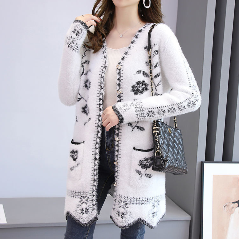 Vrouw draagt witte gebreide cardigan met zwarte bloemenprint, gecombineerd met een zwarte handtas. Modieuze dameskleding, herfststijl.