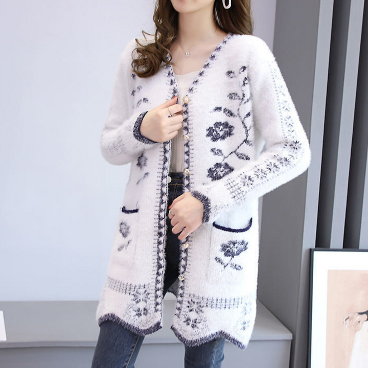Vrouw draagt witte gebreide cardigan met donkerblauw bloemenpatroon, lange mouwen en zakken. Modieuze dameskleding, herfst-winter stijl.