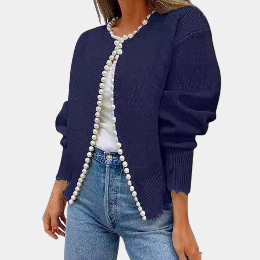 Donkerblauw damesvest met parelknopen, gecombineerd met een witte top en blauwe jeans. Modieuze casual outfit voor dames.