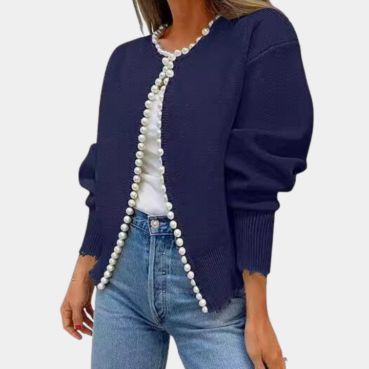 Donkerblauw damesvest met parelknopen, gecombineerd met een witte top en blauwe jeans. Modieuze casual outfit voor dames.