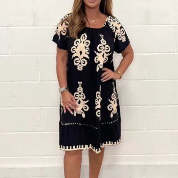 Zwarte jurk met beige bloemenpatroon, korte mouwen, gedragen door vrouw. Perfect voor zomer, casual en boho-stijl. Comfortabele pasvorm.