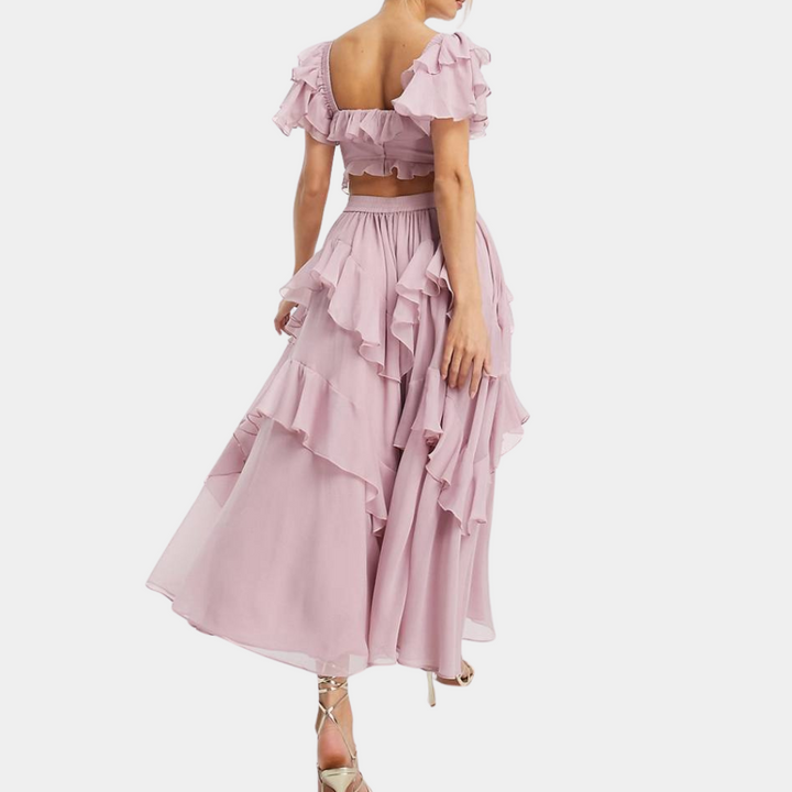 Vrouw in roze, gelaagde maxi-jurk met ruches en korte mouwen, elegante avondkleding, modetrend, zomerjurk, stijlvolle outfit.
