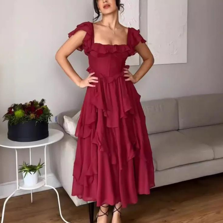 Vrouw in elegante rode jurk met ruches, staand in moderne woonkamer. Trendy avondjurk, perfecte keuze voor feestelijke gelegenheden.