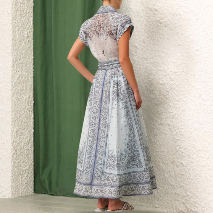 Vrouw in elegante, blauwe maxi-jurk met paisley-patroon, staand voor groene en witte achtergrond. Zomermode, bohemian stijl, dameskleding.