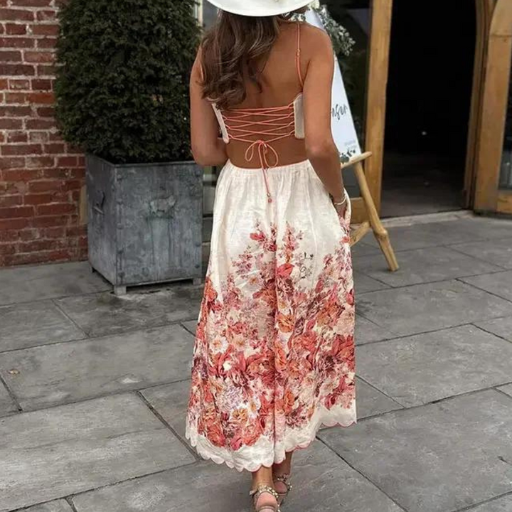 Vrouw in elegante zomerjurk met bloemenprint en open rug, wandelend op stenen terras. Perfecte outfit voor zomerse dagen en vakanties.
