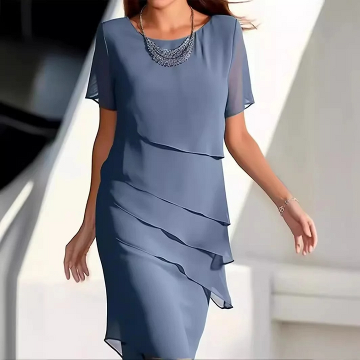 Elegante blauwe jurk met gelaagde chiffon lagen en korte mouwen, gedragen door een vrouw. Perfect voor formele gelegenheden en avondfeesten.