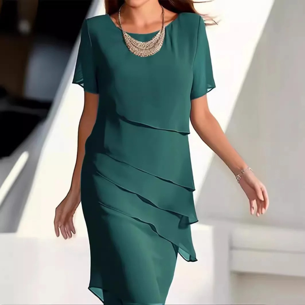 Groene jurk met gelaagde ruches, korte mouwen en ronde halslijn, gedragen door een vrouw. Perfect voor elegante zomerevenementen.