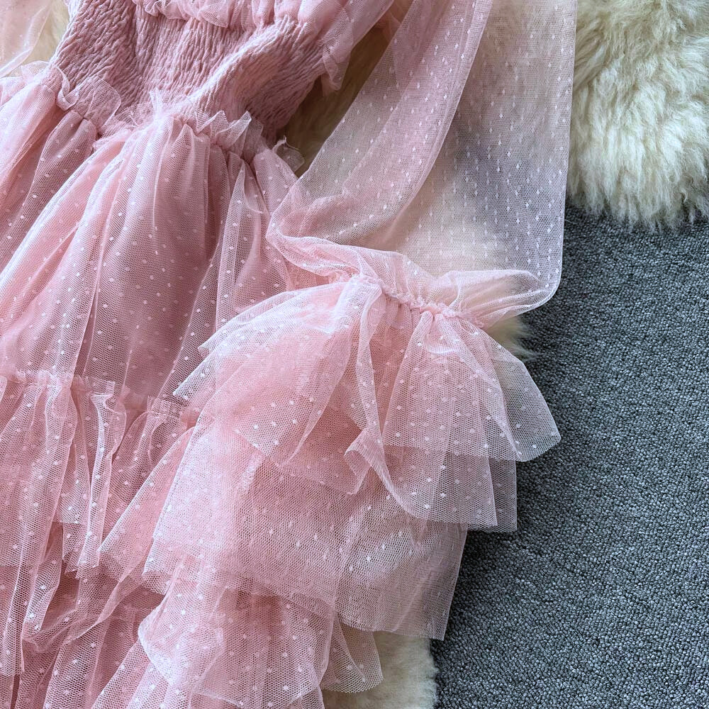 Roze tule jurk met stippen, ruches en lange mouwen op grijze achtergrond. Perfect voor feestelijke gelegenheden. Elegante damesmode.