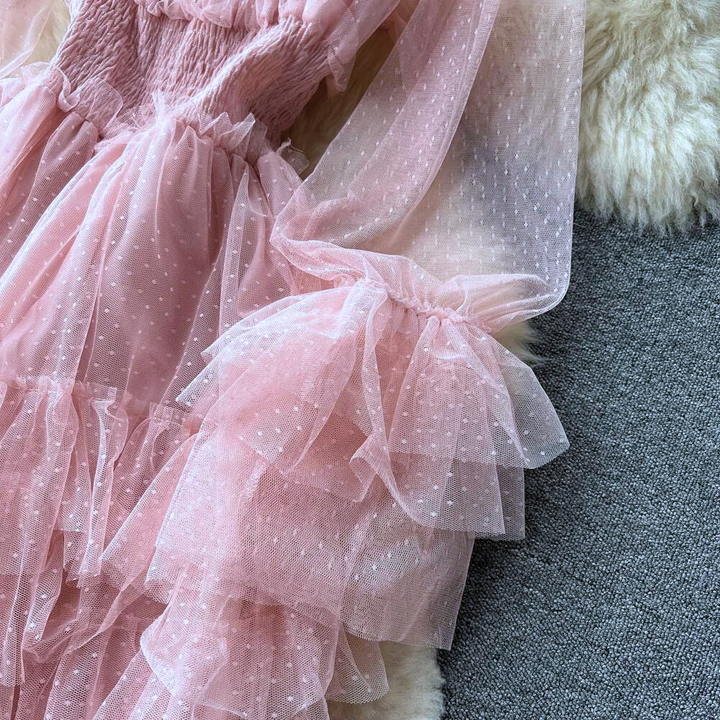 Roze tule jurk met stippen, ruches en lange mouwen op grijze achtergrond. Perfect voor feestelijke gelegenheden. Elegante damesmode.