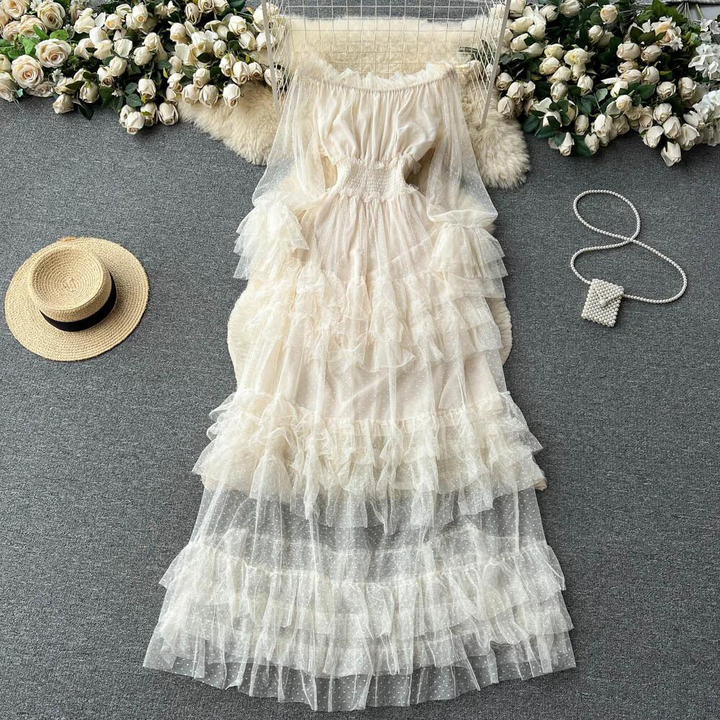 Witte, gelaagde tule jurk met ruches op grijze achtergrond, omringd door witte rozen, strohoed en parelhandtas. Perfect voor zomerse bruiloften.