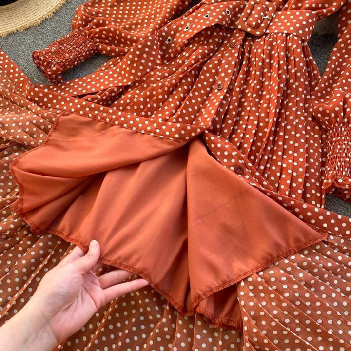 Oranje-rode jurk met witte stippen, lange mouwen en ceintuur. Hand toont binnenvoering. Modieuze dameskleding, vintage stijl.