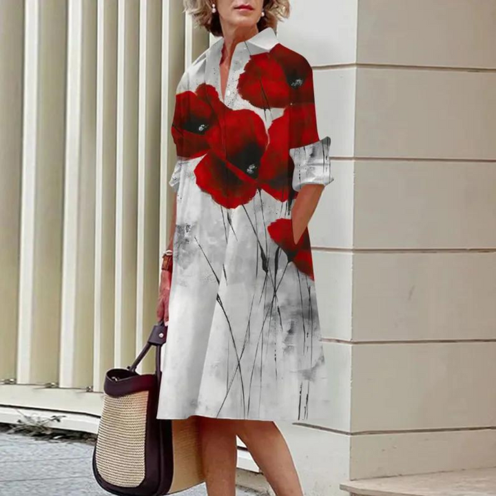Vrouw in witte jurk met rode klaprozenprint, staand bij moderne architectuur. Stijlvolle mode, casual chique, zomerkleding, stedelijke achtergrond.