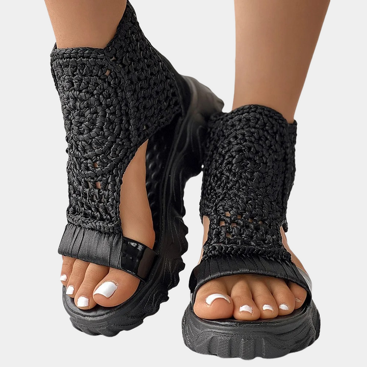 Zwarte gevlochten sandalen met dikke zool, gedragen door een persoon. Trendy zomerschoeisel, comfortabel en stijlvol voor dagelijks gebruik.