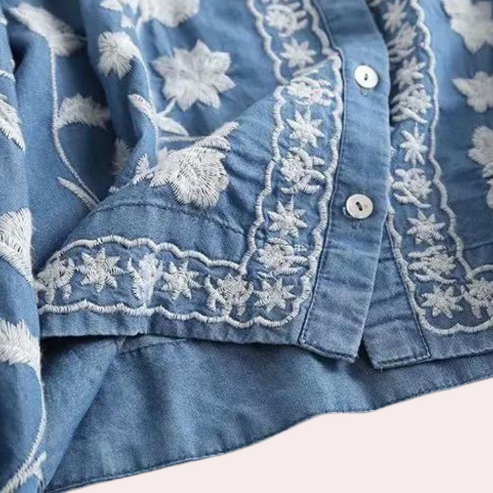 Blauwe blouse met witte bloemenborduursels, knoopsluiting en decoratieve patronen. Perfect voor casual en stijlvolle outfits.