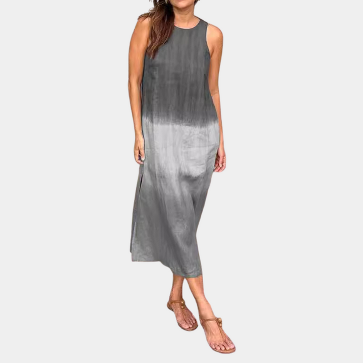 Grijze maxi-jurk zonder mouwen, casual stijl, gedragen door vrouw. Perfect voor zomer, strand, vakantie. Comfortabele en modieuze dameskleding.